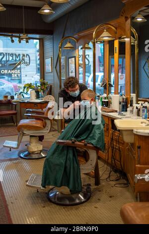 Manhattan, Kansas, USA. Mai 2020. DYLAN ROBERTS, Mitte, schneidet CALDER WEDDLE'S, 4, Haare am Mittwoch. Der Campus Barbershop in Aggieville, Kansas ältestem Einkaufsviertel, ist seit März 17 geschlossen und hat zwei Tage geöffnet. Mai 18 war der erste Tag der Phase 1.5 des Plans, Kansas Wirtschaft wieder zu öffnen. Kredit: Luke Townsend/ZUMA Wire/Alamy Live News Stockfoto