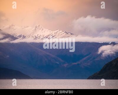 Sonnenuntergang über dem Lake Wanaka von Eely Point mit den schneebedeckten Gipfeln des Mount Aspiring National Park, Otago, South Island, Neuseeland Stockfoto