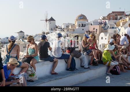 Oia, Santorini, Griechenland - 22. Juli 2014: Massen von Touristen warten auf Sonnenuntergang am Aussichtspunkt auf dem Schloss mit Windmühle und Kuppel im Hintergrund Stockfoto