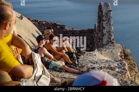 Oia, Santorini, Griechenland - 22. Juli 2014: Junge Touristen sitzen und warten auf den Sonnenuntergang am Aussichtspunkt auf der Burg Stockfoto