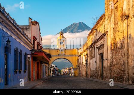 Der Santa Catalina Arch in der Hauptstraße von Antigua City ohne Menschen und der Agua Vulkan im Hintergrund bei Sonnenaufgang, Guatemala. Stockfoto