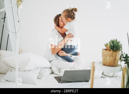 Nettes Kleinkind Mädchen mit langen fairen Haaren Spaß mit Mutter auf dem Bett in hellen Innenraum Stockfoto