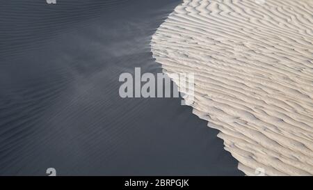 Wind weht Sand an der Spitze einer Sanddüne. Abstraktes Bild, das helle und dunkle Seiten zeigt Stockfoto