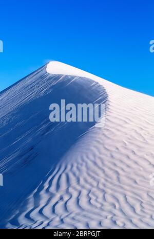 Wind weht Sand an der Spitze einer Sanddüne. Abstraktes Bild, das helle und dunkle Seiten zeigt Stockfoto