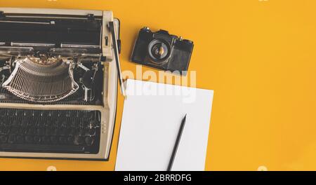 Schreibmaschine, Retro-Filmkamera, Blatt Papier und Bleistift auf gelbem Hintergrund, Draufsicht mit Kopierraum. Kreatives Konzept Stockfoto
