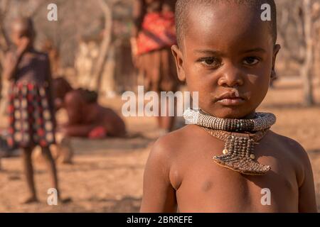 Land Namibia - 21. August 2016. Ein kleiner Junge, der Stammesketten in einem abgelegenen Himba Dorf trägt, hat eine laufende Nase von einer Erkältung. Stockfoto