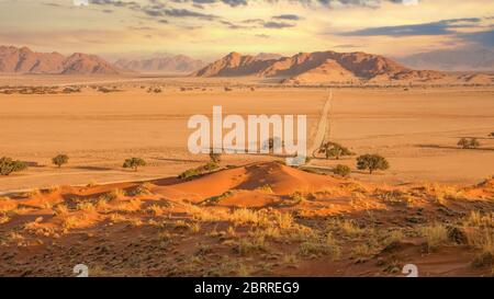 Ein schöner Panoramablick, Sonnenuntergang Blick auf die Namib Wüste, wo eine lange Feldweg durchquert ein Tal zwischen Bergen im Hintergrund und dem roten Sand d Stockfoto