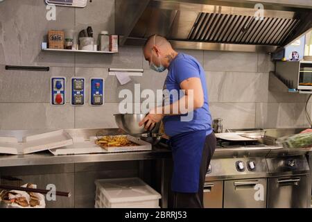 Der Besitzer eines Delikatessenladen und Pizzeria, um in seinen Räumlichkeiten zur Wiedereröffnung der kommerziellen Tätigkeit zu nehmen. Vorbereitung einer Pizza vor der Lieferung. Stockfoto