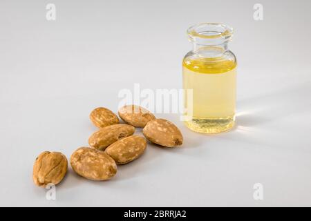 Glas mit Öl und einer Gruppe geschälter Mandelkerne auf einer weißen Oberfläche Stockfoto