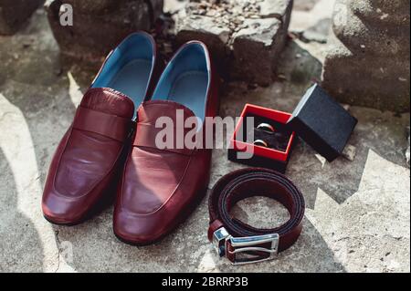Herrenschuhe, Gürtel und Eheringe von Cherry in einer Schachtel. Accessoires des Bräutigams am Hochzeitstag Stockfoto
