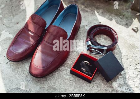 Herrenschuhe, Gürtel und Eheringe von Cherry in einer Schachtel. Accessoires des Bräutigams am Hochzeitstag Stockfoto