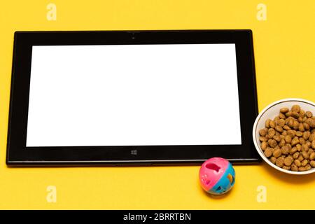Kaufen Sie Tiernahrung und Spielzeug online über die App auf Ihrem Tablet, auf einem gelben Hintergrund mit einer Kopie des Raumes. Das Konzept des Online-Shopping, elektronische p Stockfoto
