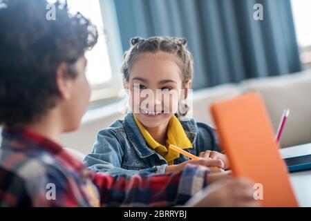 Lockiger Junge und dunkelhaariges Mädchen sitzen am Tisch, tun ihre Aufgaben, diskutieren etwas, genießen die Zeit zusammen Stockfoto