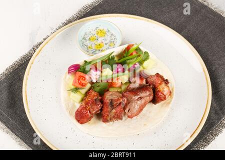 Schweinespieße, die in einem josper-Ofen gekocht werden. Serviert auf einem Teller mit Pita Brot, Gemüse und Sauce. Stockfoto