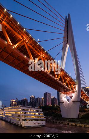 Chongqing, China - August 2019 : hell erleuchtetes riesiges Passagierschiff, das unter der DongShuiMen Brücke am Zusammenfluss von Yangtze und Jialing riv fährt Stockfoto