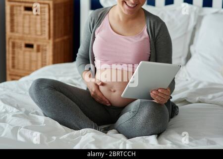 Nicht erkennbare schwangere Frau mit Tablette im Bett Stockfoto