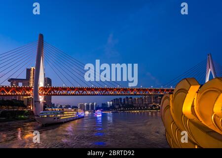 Chongqing, China - August 2019 : hell erleuchtetes riesiges Passagierschiff, das unter der DongShuiMen Brücke am Zusammenfluss von Yangtze und Jialing riv fährt Stockfoto