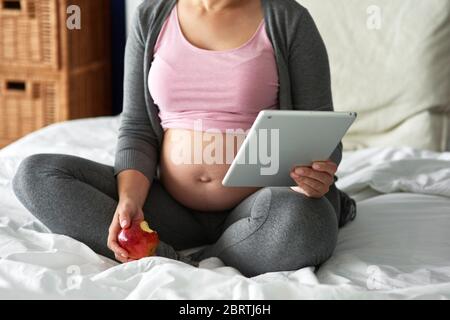 Nicht erkennbare schwangere Frau mit Tablet während im Bett sitzen Stockfoto
