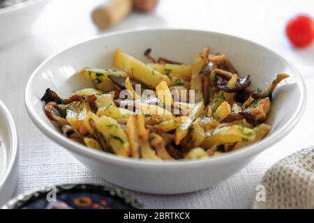 Gebratene Kartoffeln gebraten mit Steinpilzen wild auf weißen Teller und Frühlingszwiebeln auf Holztisch Hintergrund Stockfoto