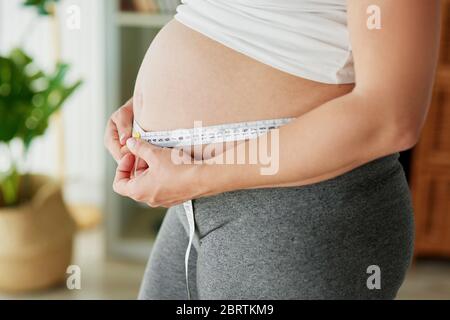 Schwangere Frau mit Maßband, um den Bauch zu kontrollieren Stockfoto