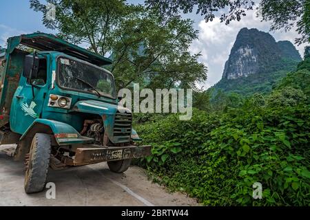 Yangshuo, China - August 2019 : alter rostiger Transporter, der auf einer Seite einer schmalen Bergstraße zwischen dem beeindruckenden und beeindruckenden Bergkar geparkt wurde Stockfoto