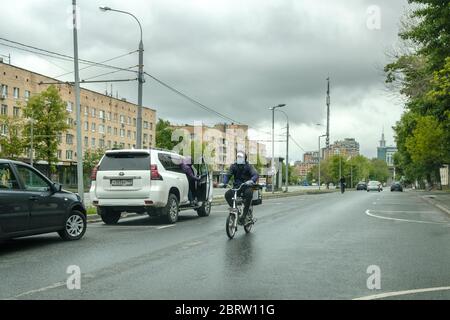 Moskau, Russland. 21.Mai 2020. Ein Kurier in einer Schutzmaske fährt an einem bewölkten Tag ein Fahrrad auf einer Straße in einer Stadt. Lieferung von Lebensmitteln für Quarantäne coro Stockfoto