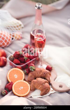 Ein Glas Roséwein mit Erdbeere und Obst und Croissants auf Holztablett im Freien Nahaufnahme. Picknick-Zeit. Sommersaison. Urlaub. Stockfoto