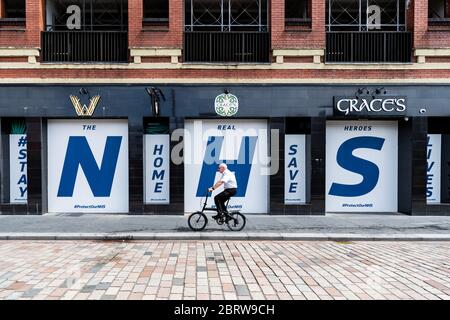 Coronavirus Lockdown - ein älterer Radler passiert ein riesiges "NHS Stay Home Save Lives" Schild in den Fenstern des geschlossenen Pubs - Glasgow, Schottland, Großbritannien Stockfoto