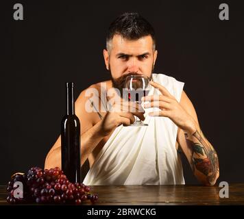 Sommelier riecht Getränk. Gott Bacchus mit ernsten Gesicht trägt weißes Tuch sitzt von Weinflasche und Trauben. Mann mit Bart hält Glas Wein auf braunem Hintergrund. Weinbereitung und Degustationskonzept Stockfoto