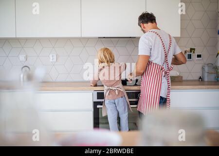 Ein Rückansicht des kleinen Jungen mit Vater drinnen in der Küche, die Pfannkuchen macht. Stockfoto