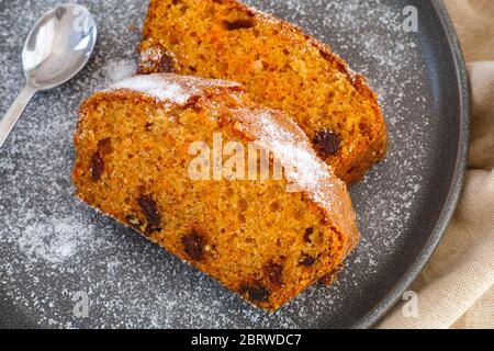 Zwei Stücke Karottenkuchen mit Rosinen auf grauem Teller mit Löffel. Stockfoto