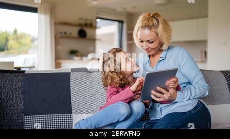 Ein nettes kleines Mädchen mit Mutter auf dem Sofa zuhause, mit Tablet. Stockfoto