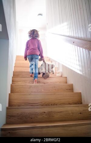 Ein Blick von hinten auf kleine Mädchen, die Holztreppe zu Hause hinauf. Stockfoto