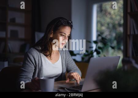 Eine Geschäftsfrau mit Laptop sitzt im dunklen Büro drinnen am Schreibtisch. Stockfoto