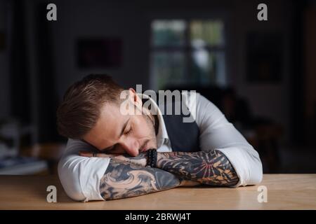 Müde junge Geschäftsmann sitzt am Schreibtisch im Büro drinnen und schläft. Stockfoto