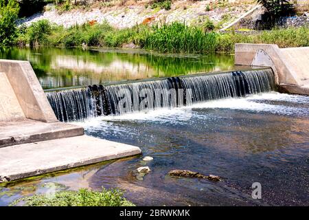 Wasserkaskade, die von einem kleinen Damm herabströmt, wassersparendes ökologisches Konzept. Stockfoto