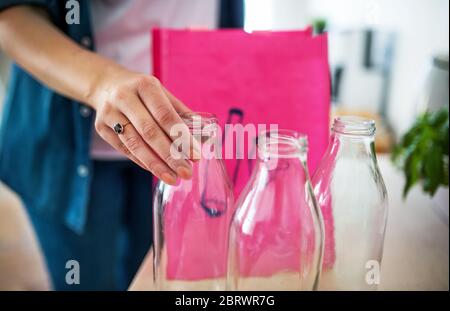 Junge Frau, die Glasflaschen zuhause in die Tasche stecken, Recycling-Konzept. Stockfoto