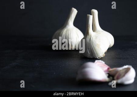 Knoblauchzehen und unfokussierte Knoblauchköpfe auf schwarzem Hintergrund. Dunkle Nahrung Stockfoto