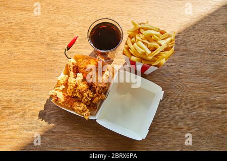 Draufsicht auf frittierten Hähnchen, pommes Frites und Soda im Glas auf Holztisch bei Sonnenlicht Stockfoto