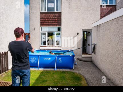 North Berwick, East Lothian, Schottland, Großbritannien, 22. Mai 2020. Spendensammeln Schwimmen im Planschbecken: Jane McMenemy, 40 Jahre, schwimmt 5 Meilen in ihrem Vorgarten, der an eine Widerstandsband gebunden ist, um Geld für den Zoo von Edinburgh während der Sperre des Coronavirus-Covid-19 zu sammeln. Ihr Ziel von £500 wurde erreicht, bevor das Schwimmen begann. Die Pools sind 10 Meter lang und 75 cm tief. Bei 1 Meile pro halbe Stunde sollte es 2.5 Stunden dauern, bis das Ziel erreicht ist. Ihr Mann, Scott, filmt die Veranstaltung Stockfoto