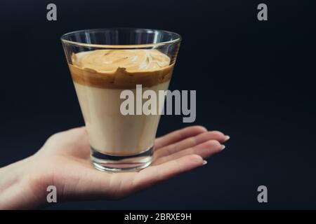 Frau Hand hält trendy koreanischen Dalgona Kaffee zu Hause gemacht. Schwarzer Boden Stockfoto