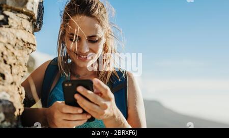 Frau, die beim Bergwandern das Handy benutzt. Bergsteigerin, die beim Bergsteigen auf ihr Handy schaut. Stockfoto