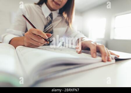 Kurze Aufnahme eines Mädchens, das sich Notizen in ihrem Buch macht, während sie in ihrem Klassenzimmer studiert. Schwerpunkt in der Hand einer Studentin, die in der Schule im Lehrbuch schreibt. Stockfoto