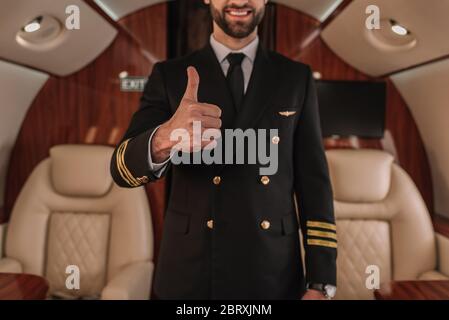 Zugeschnittene Ansicht des lächelnden Piloten des Privatjets, der den Daumen nach oben zeigt Stockfoto
