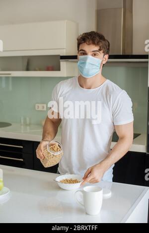 Kranker Mann in medizinischer Maske macht Cornflakes zum Frühstück in der Küche auf Selbstisolierung Stockfoto