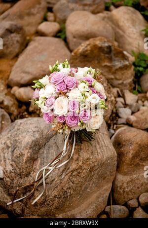 Hochzeitsstrauß in violetten und weißen Tönen von Rosen und Eustoma, fotografiert auf Steinen Stockfoto