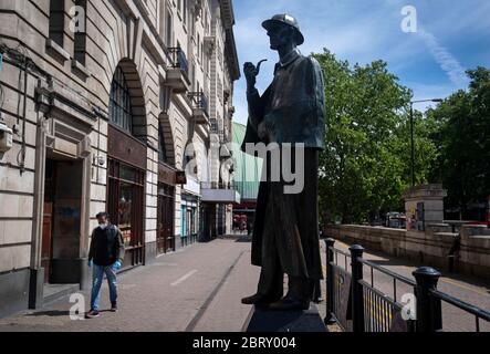 Ein Mann in einer Gesichtsmaske geht am Sherlock Holmes Day vor der U-Bahnstation Baker Street an der Sherlock Holmes Statue vorbei, nachdem Maßnahmen eingeführt wurden, um das Land aus der Blockierung zu bringen. Stockfoto