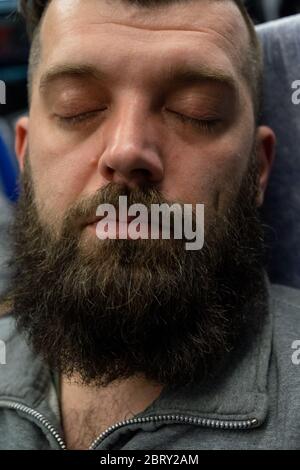 Junger Mann, der auf einem Zug am Fenster sitzt.EIN Mann mit Bart fährt auf einem Zug. Der Typ schläft. Reisen Stockfoto