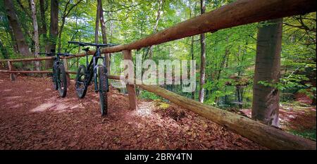 Zwei Mountainbikes auf einem Holzzaun neben einem schönen kleinen See auf einem grünen Waldweg. Mountainbike-Konzept. Freiheitskonzept. Stockfoto