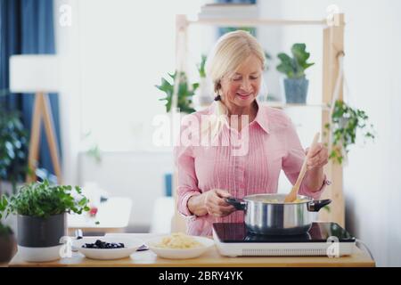 Ältere Frau, die in der Küche im Haus kocht, unter Rühren von Pasta im Topf. Stockfoto